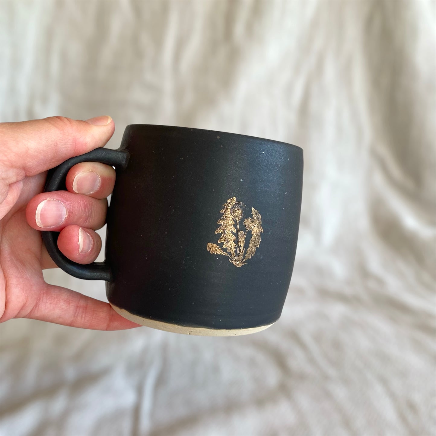 Black mug with a gold design held by a hand against a white background