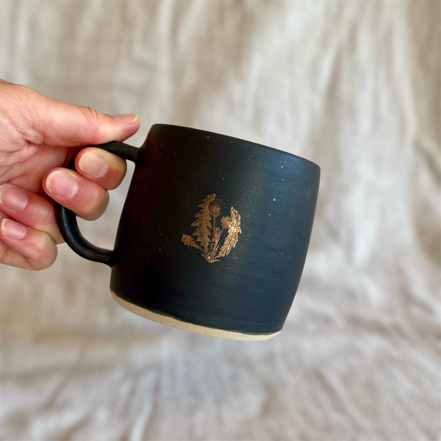 Black mug with a logo held by a hand against a light fabric background