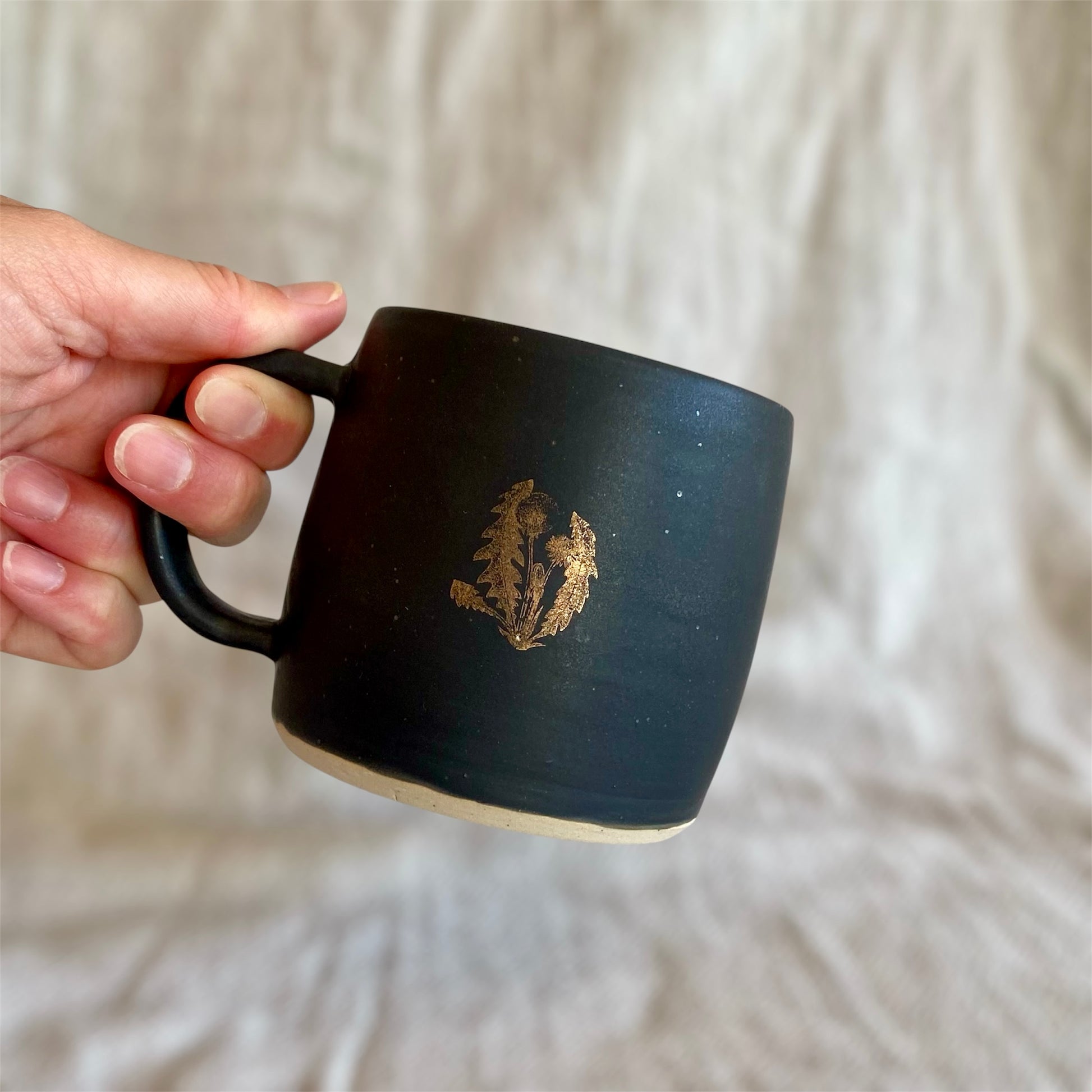 Black mug with a logo held by a hand against a light fabric background