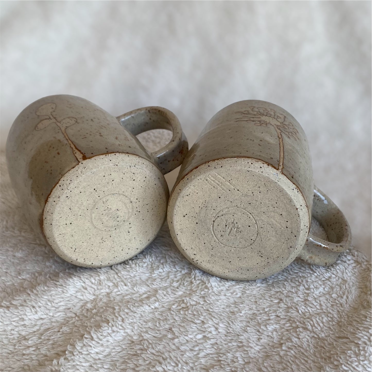 Two ceramic mugs with speckled texture on a textured surface