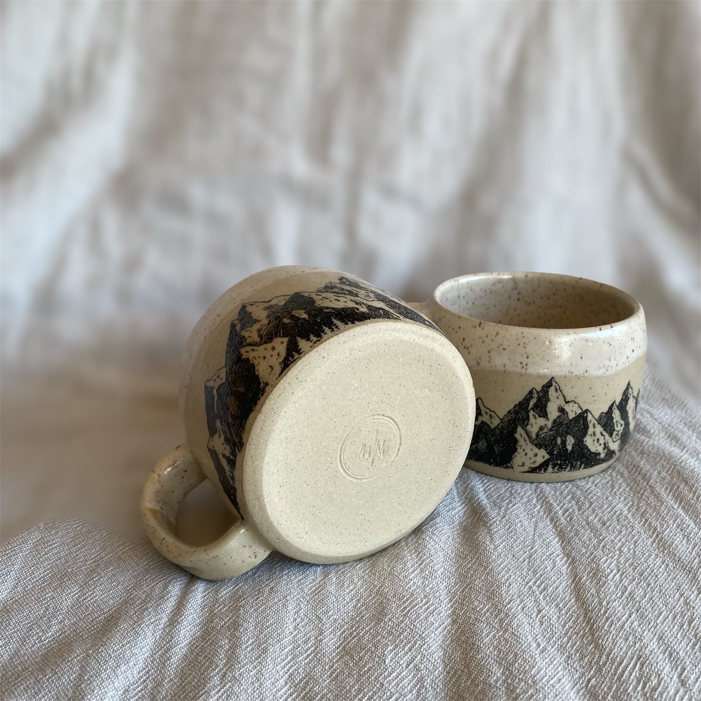 Two ceramic mugs with mountain designs on a textured surface