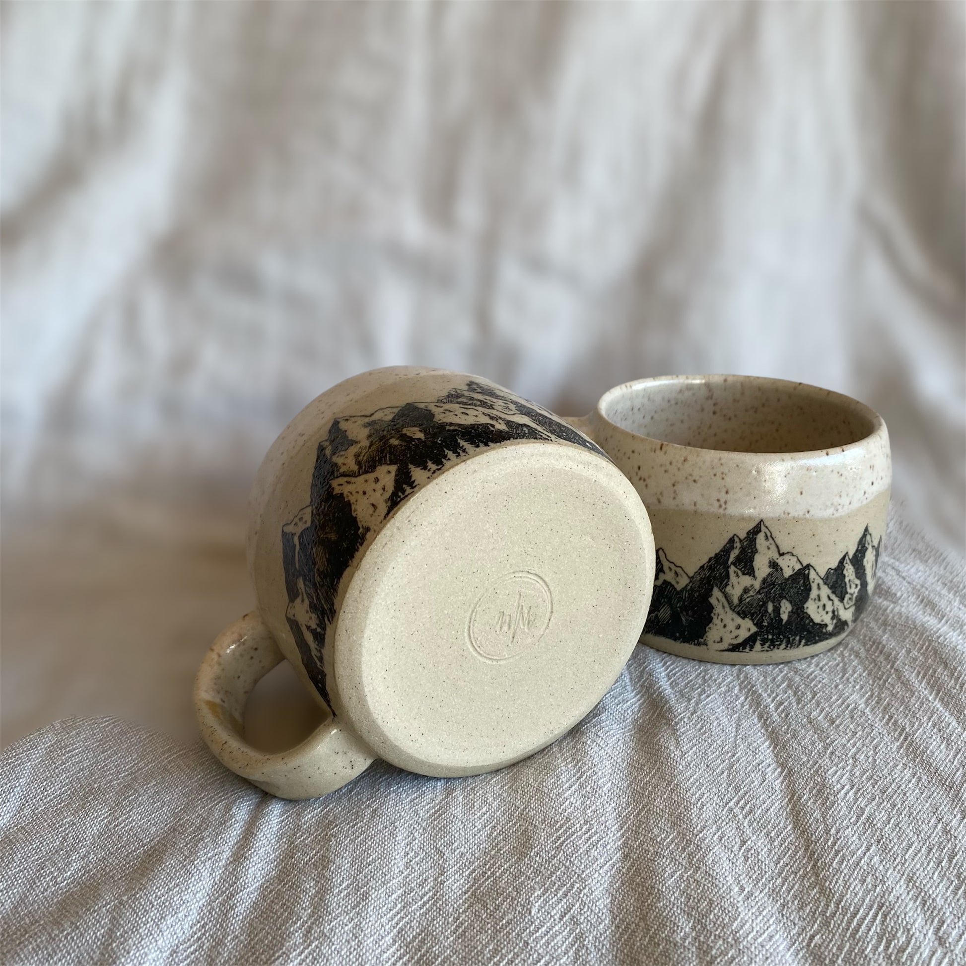 Two ceramic mugs with mountain designs on a textured surface