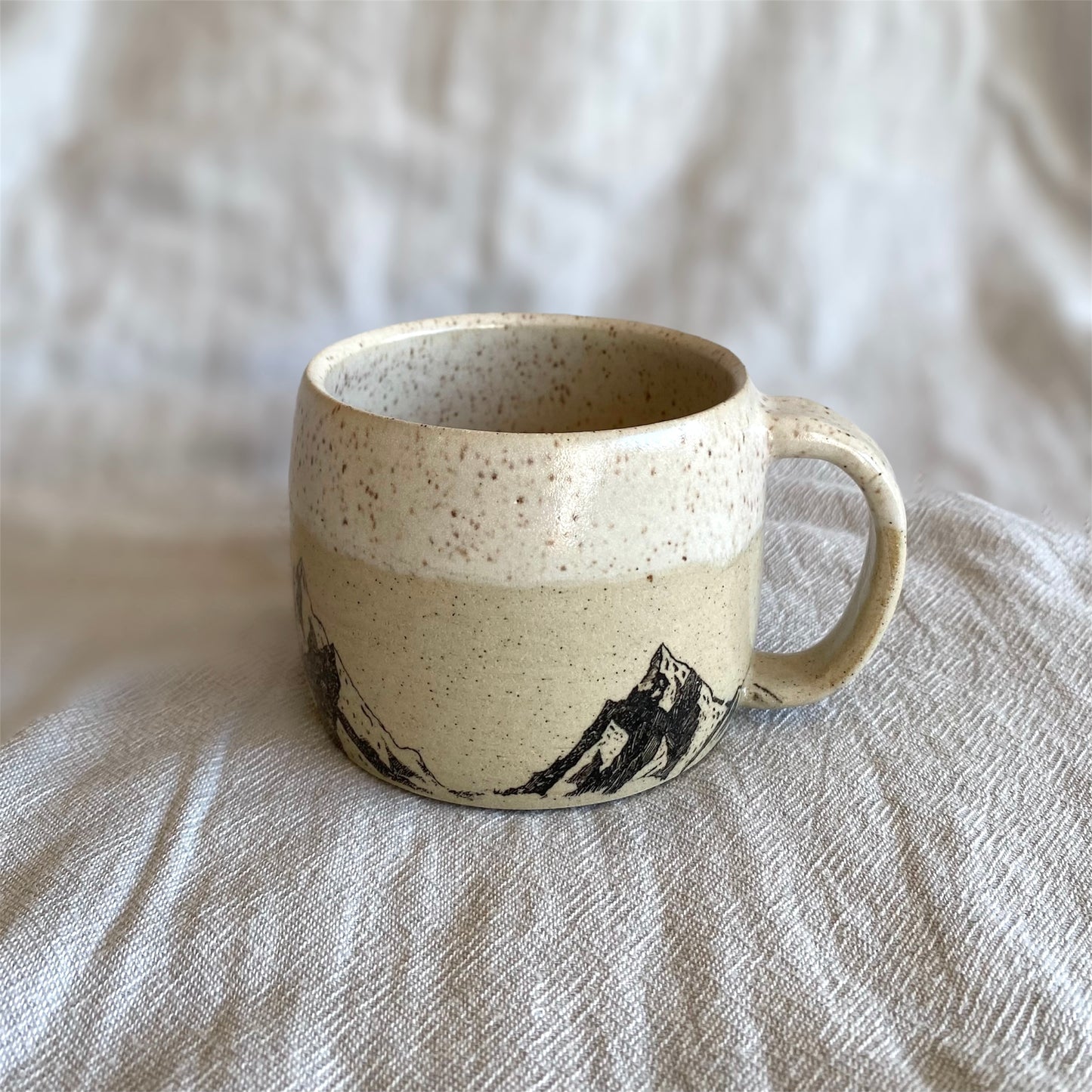 Speckled ceramic mug with a handle on a textured beige surface