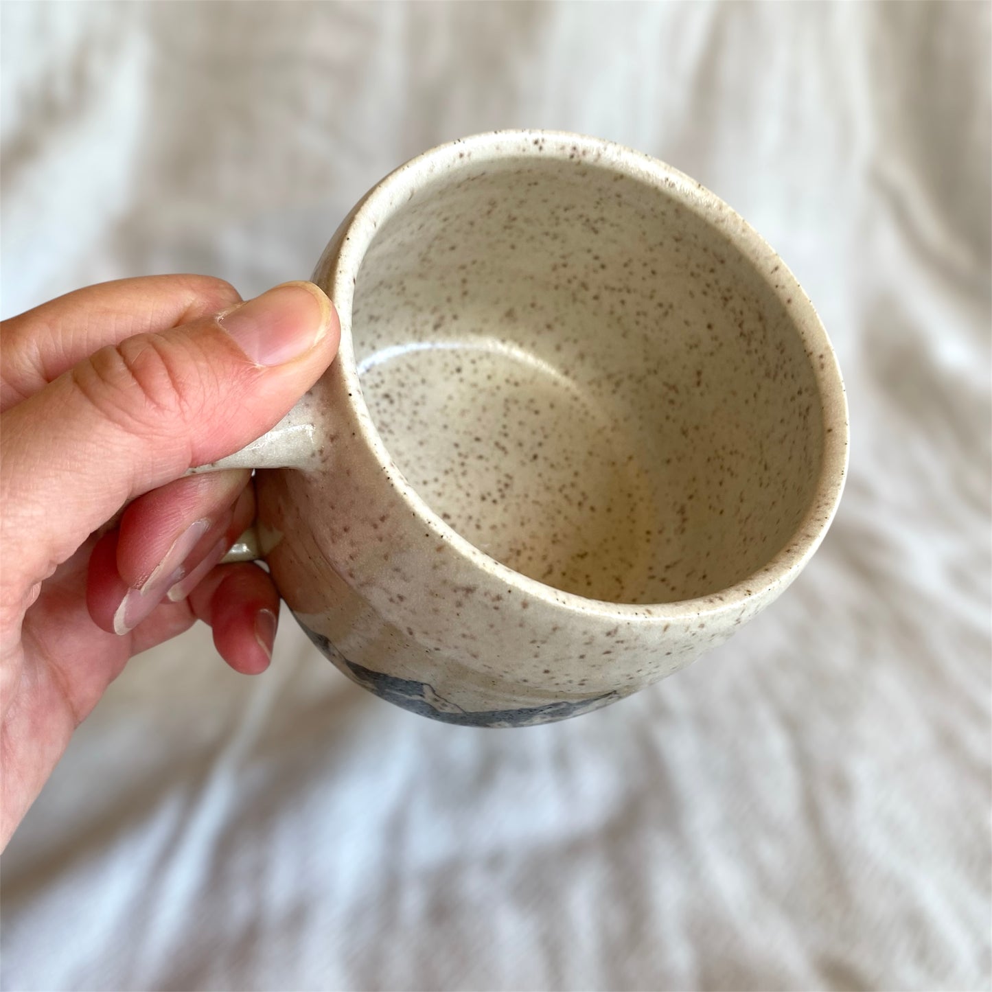 Hand holding a speckled ceramic mug against a neutral background