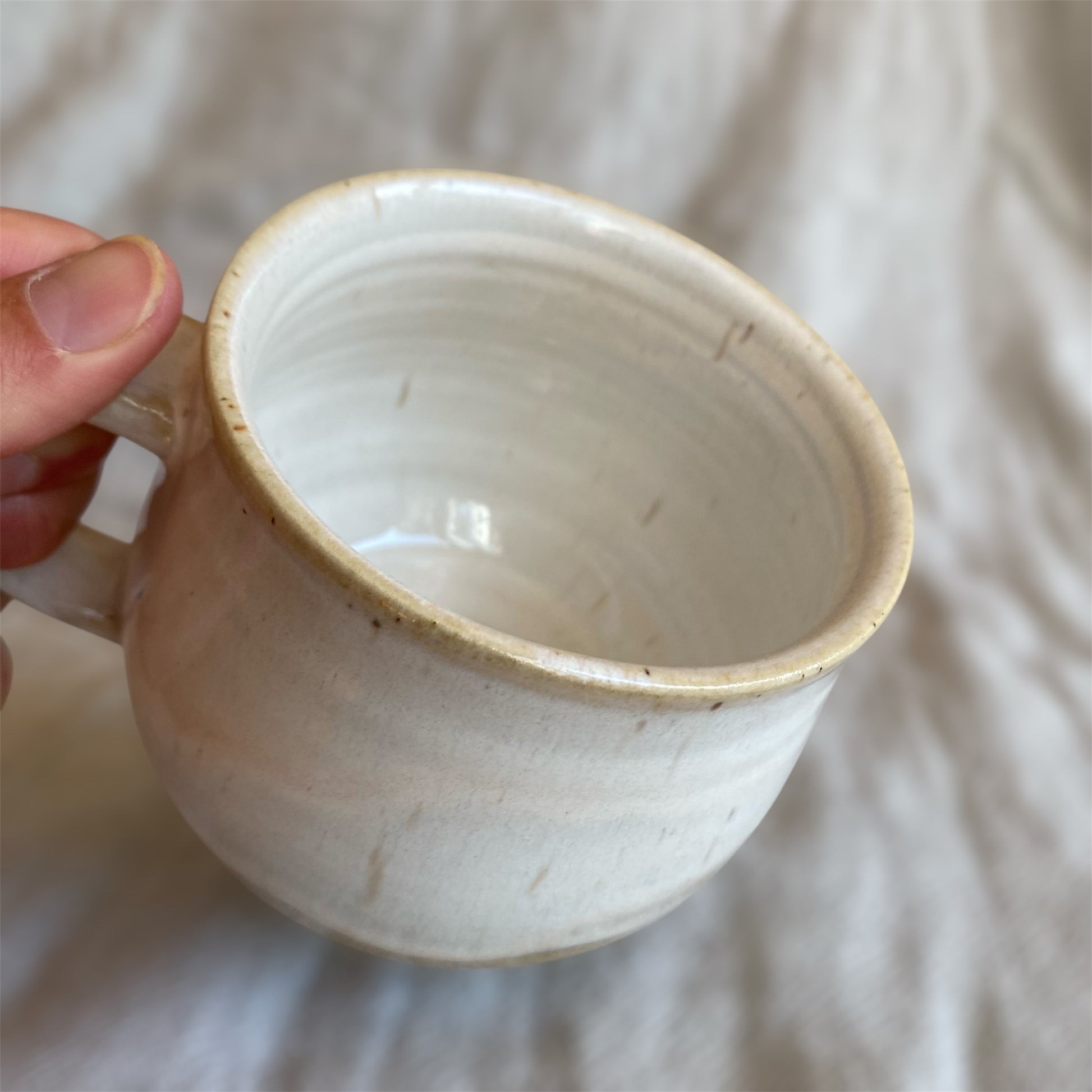 Hand holding a ceramic mug with a textured surface on a soft fabric background