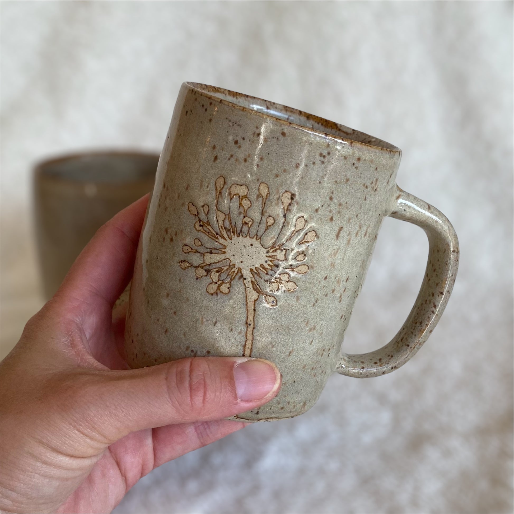Hand holding a ceramic mug with a floral design against a neutral background