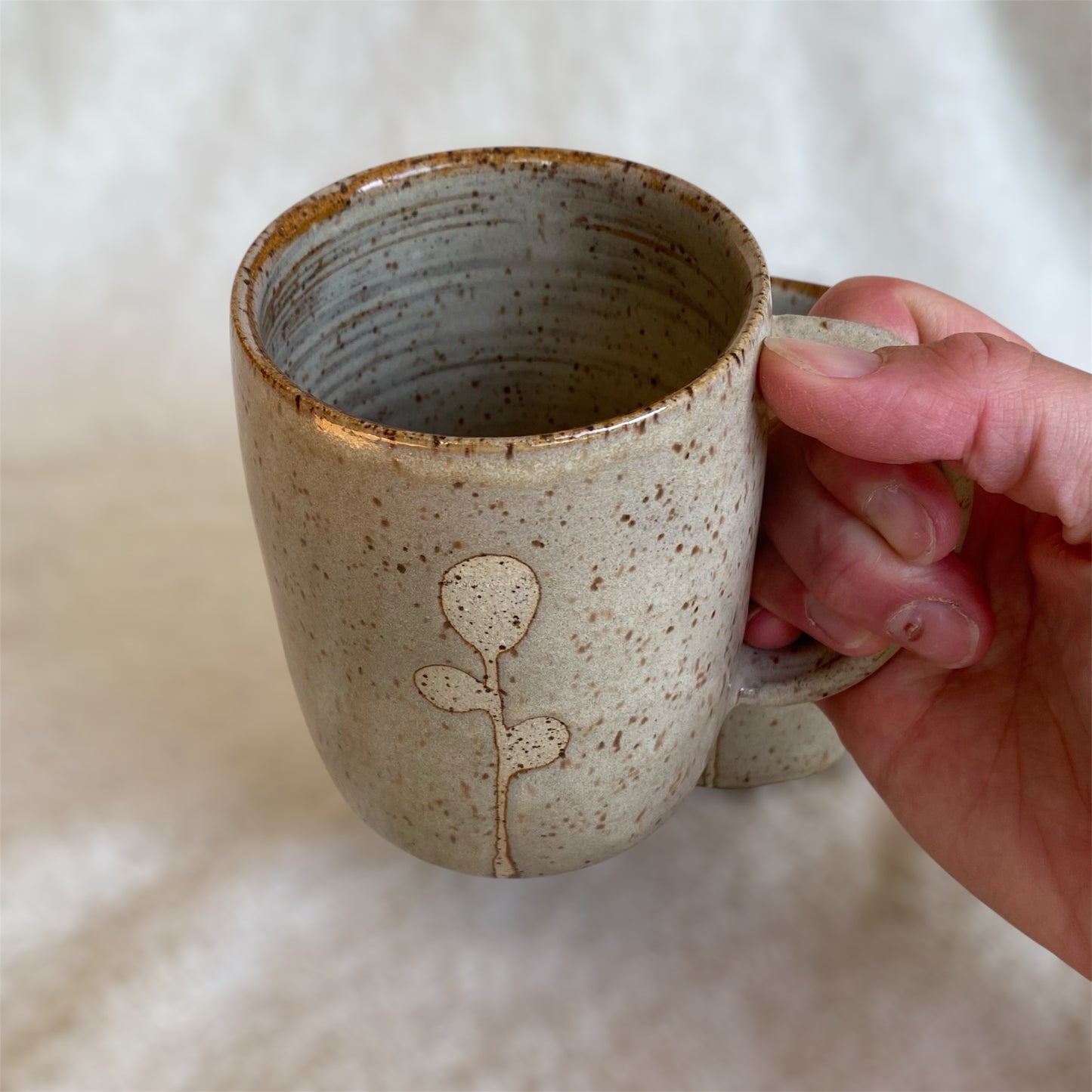 Hand holding a ceramic mug with a subtle design on a neutral background