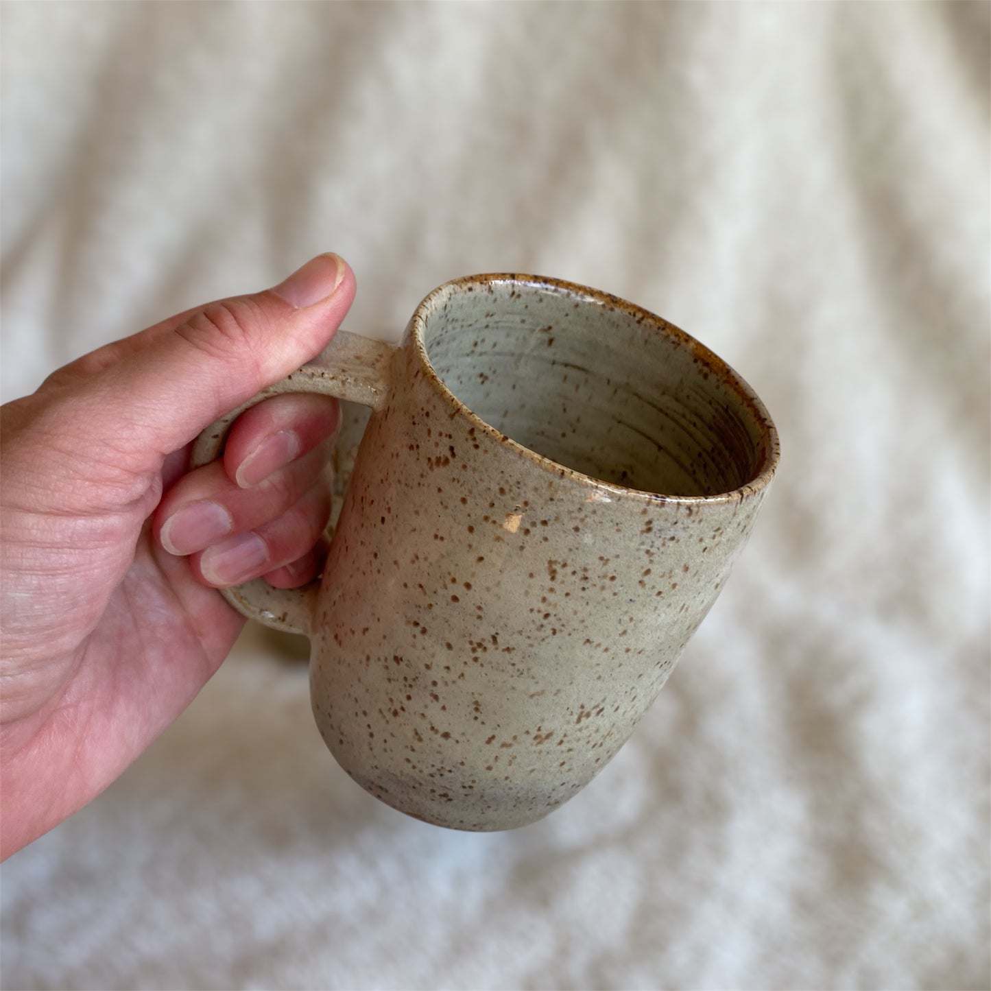 Hand holding a ceramic mug with a speckled texture against a neutral background