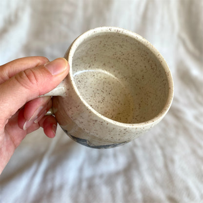 Hand holding a speckled ceramic mug against a neutral background