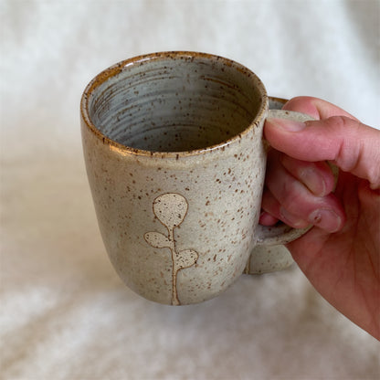 Hand holding a ceramic mug with a subtle design on a neutral background