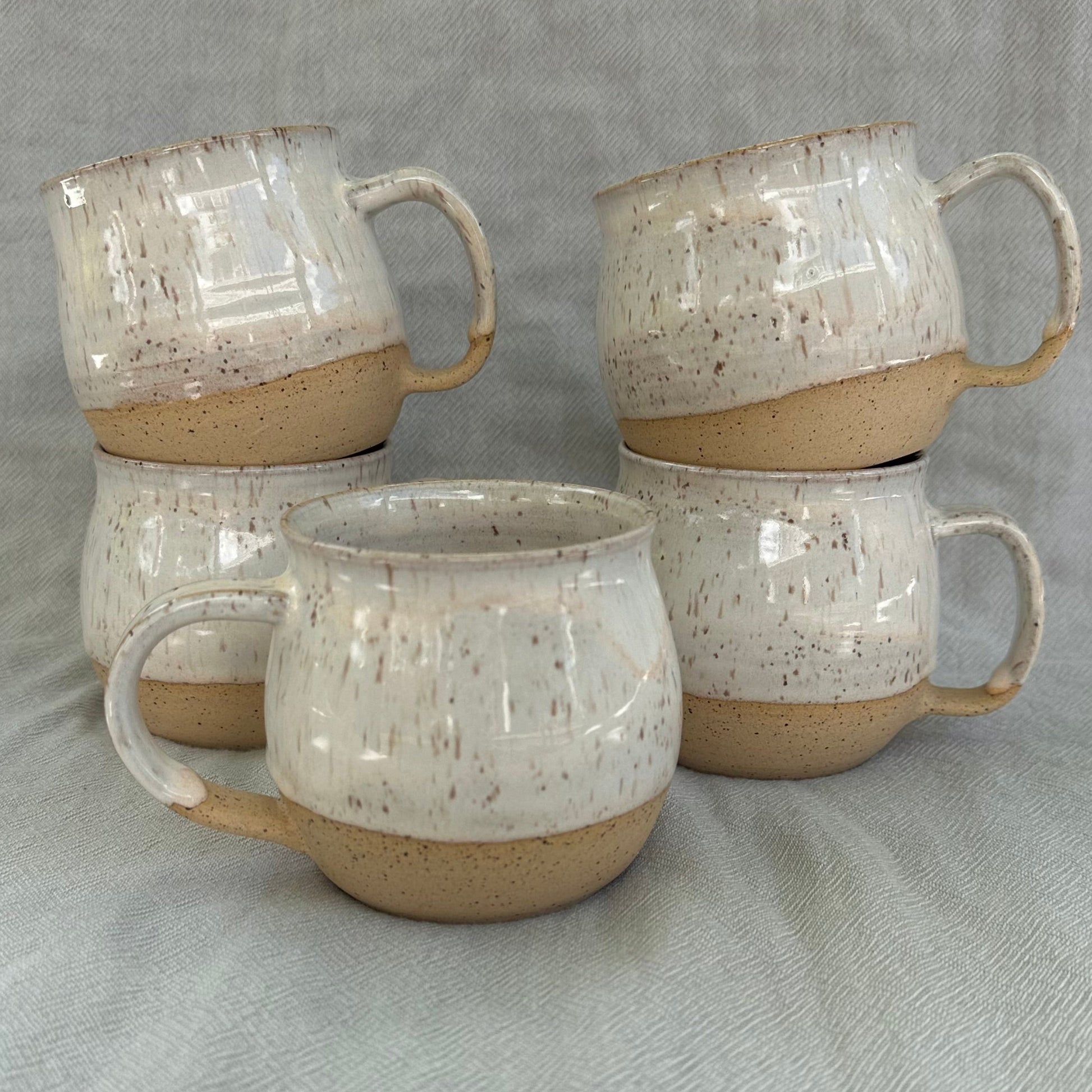 Set of four ceramic mugs with speckled glaze on a gray fabric background