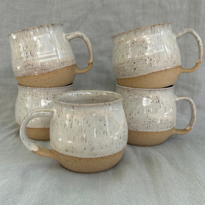 Set of four ceramic mugs with speckled glaze on a gray fabric background