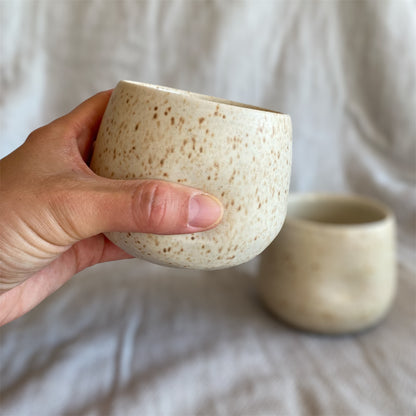 Hand holding a textured ceramic cup with another cup in the background on a neutral surface